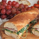 Baguette sandwich on a wooden serving tray with red grapes in the background