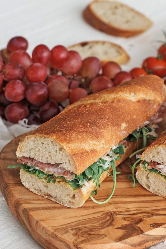 Baguette sandwich on a wooden serving tray with red grapes in the background