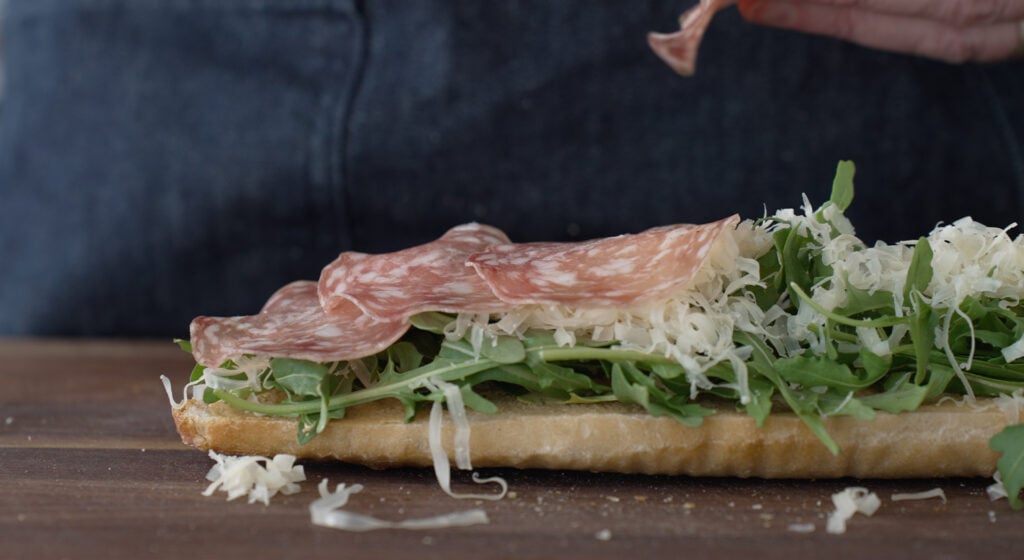 Side view of the sandwich with Arugula spread over the bottom of the baguette followed by cheese and salami
