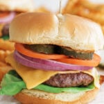 Cheese burger on a bun with pickles, tomatoes, red onion and lettuce showing