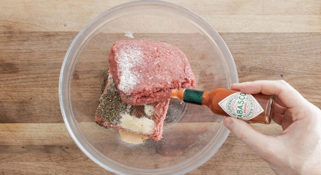 sprinkling tabasco sauce on ingredients in a glass mixing bowl 