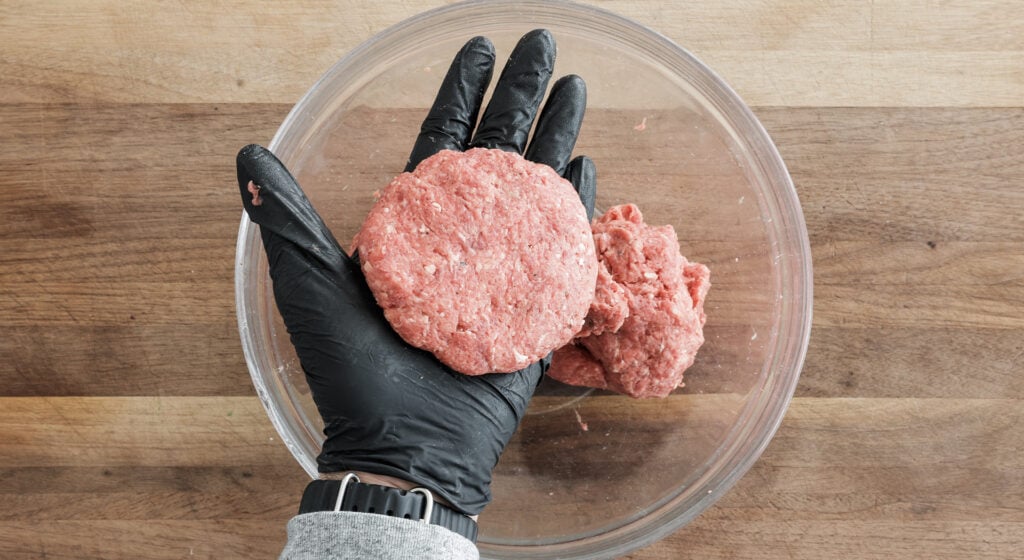 A black gloved hand holding one round burger patty