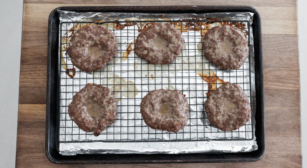 6 browned burger patties on a rack over a sheet tray lined with foil 