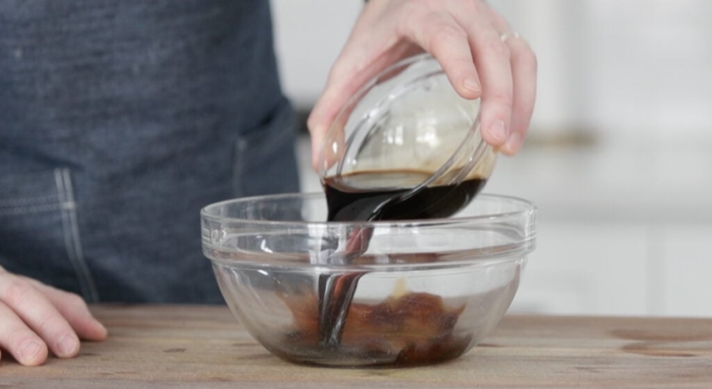 pouring balsamic vinegar into a bowl with herbs