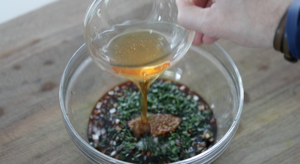 slowly pouring in oil to a bowl with vinegar while whisking