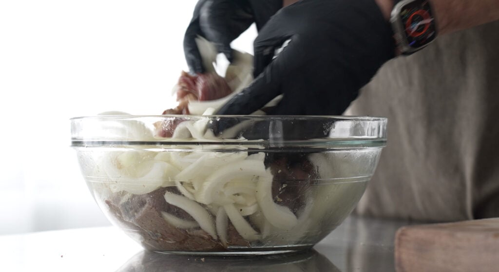 gloved hands mixing onions into the bowl with meat