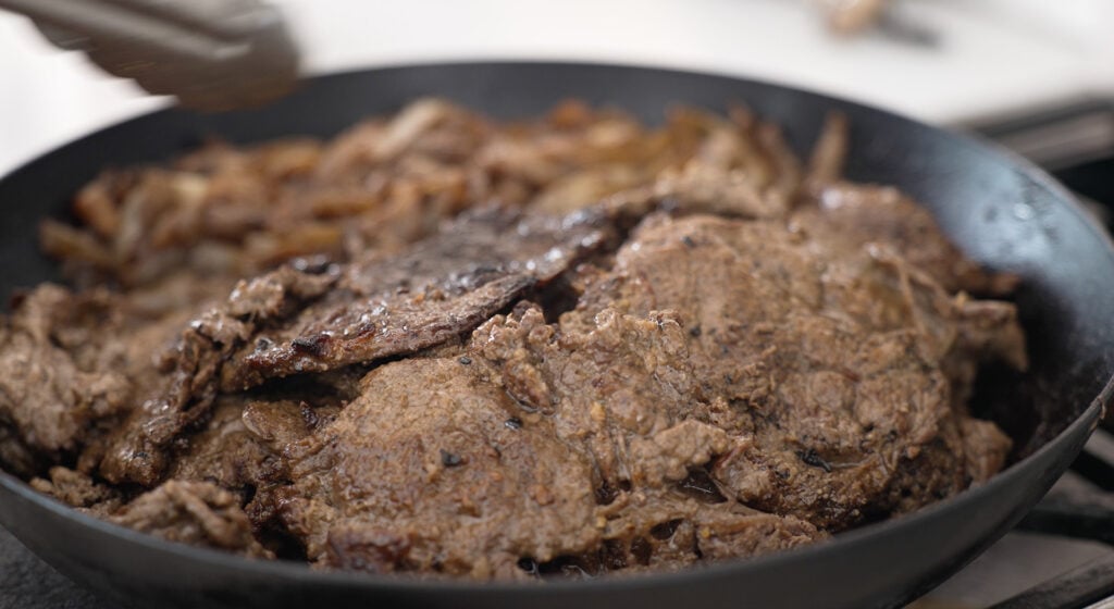 a pan with Cooked beef and onions behind it