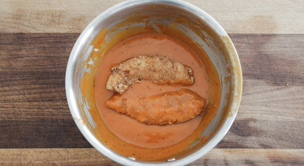 Fried chicken tenders in a large bowl of buffalo sauce