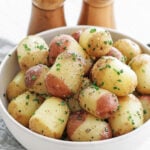 Steamed buttered potatoes in a white serving bowl with a wooden salt and pepper shaker behind
