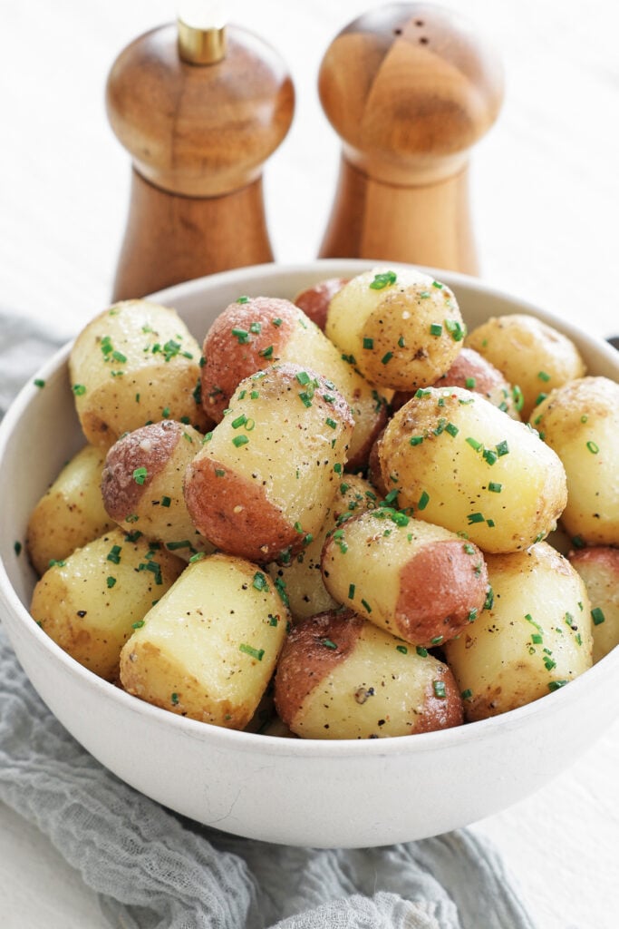 Steamed buttered potatoes in a white serving bowl with a wooden salt and pepper shaker behind