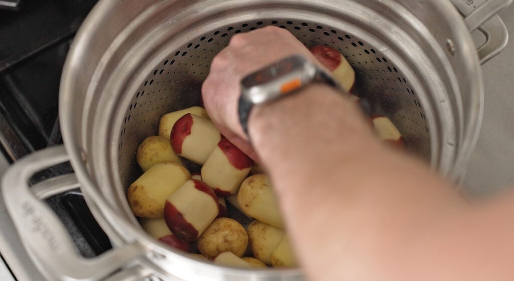 A hand placing potatoes into the basket in the pot