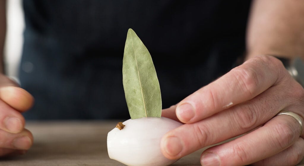 Close up of bay leaf and clove stuck in a shallot