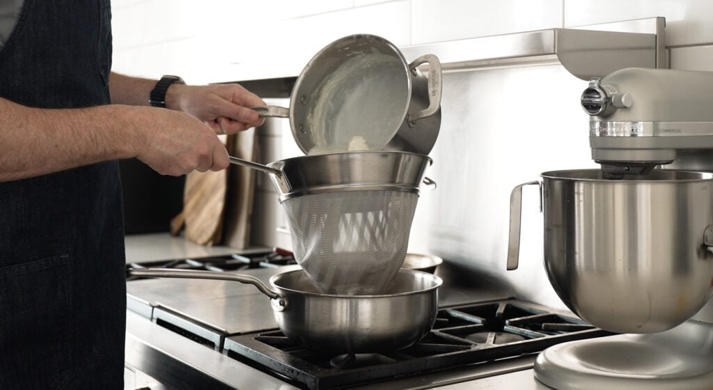 pouring contents of pot through a fine mesh strainer over another pan