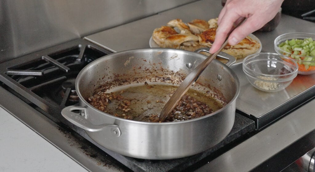 Browned onions being stirred with a wooden kitchen utensil on the stove