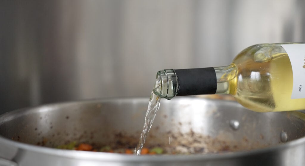pouring white wine into a pan