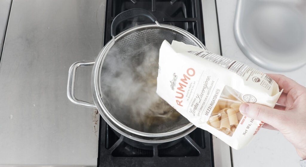 pouring pasta into a large pot with a basket insert 