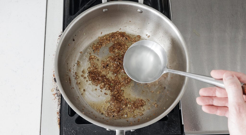 using a ladle to add pasta water to a pot