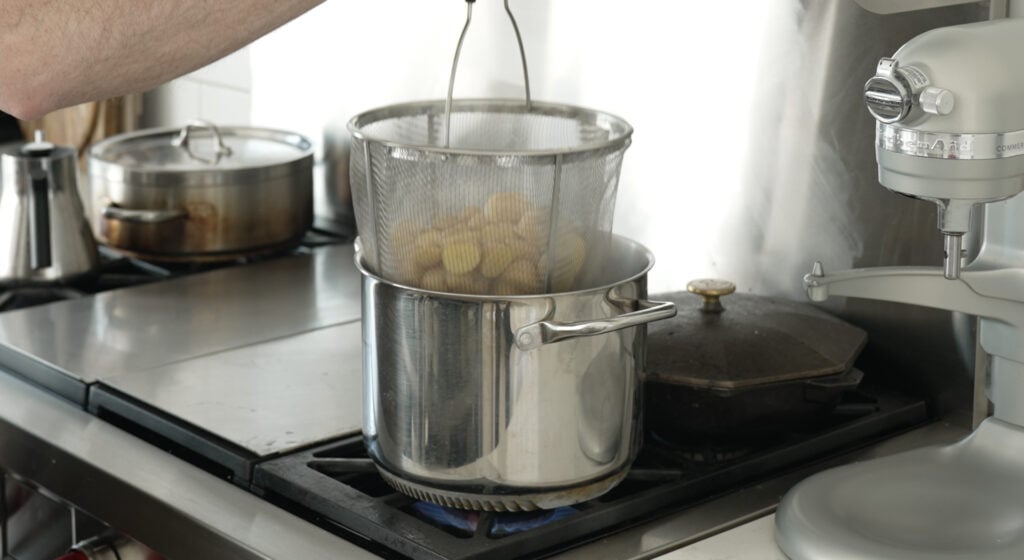 pulling a steamer basket with potatoes from a pot on the stove