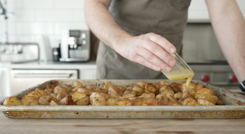 Drizzling melted putter over the potatoes on a sheet tray
