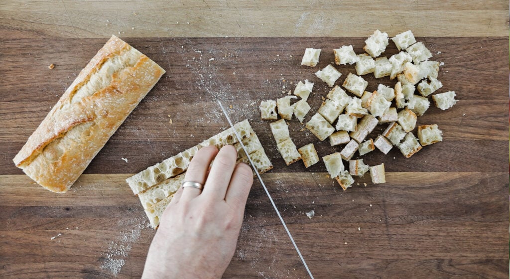 cutting a baguette into small bite-size pieces on a cutting board