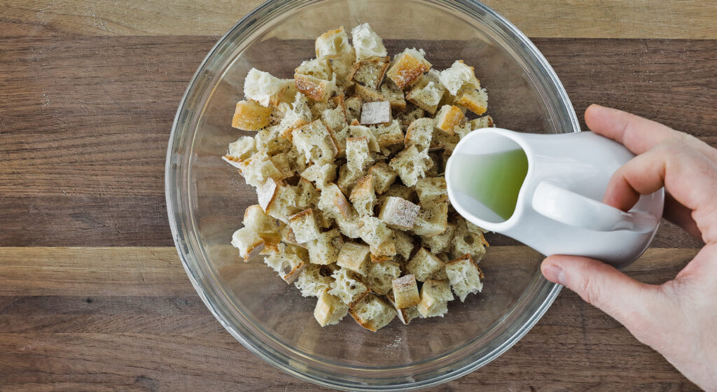 adding olive oil to a bowl full of small cubed bread