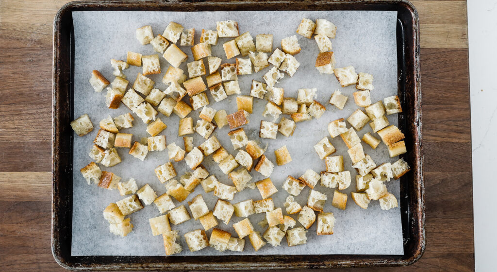 croutons spread out on a cookie sheet tray with parchment paper