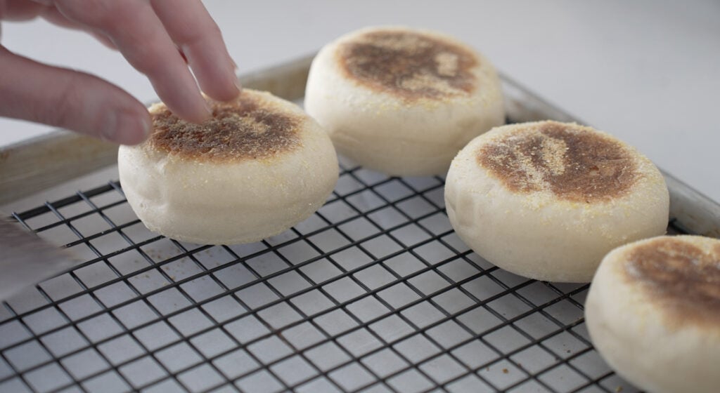 Browned english muffins cooling on a wire rack over a sheet tray