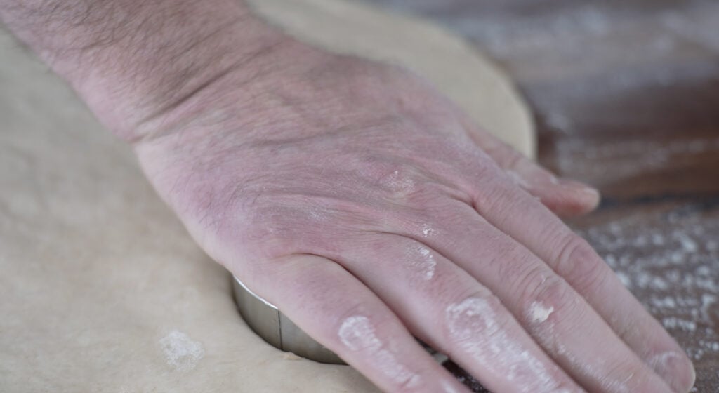 hand pressing down on cutter, cutting dough