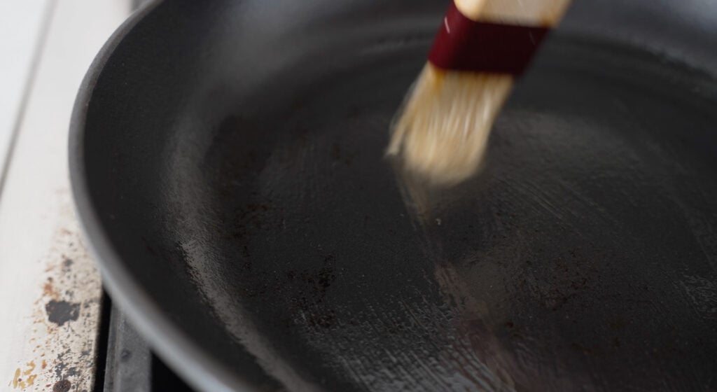 Using a brush to apply oil to a cast iron pan