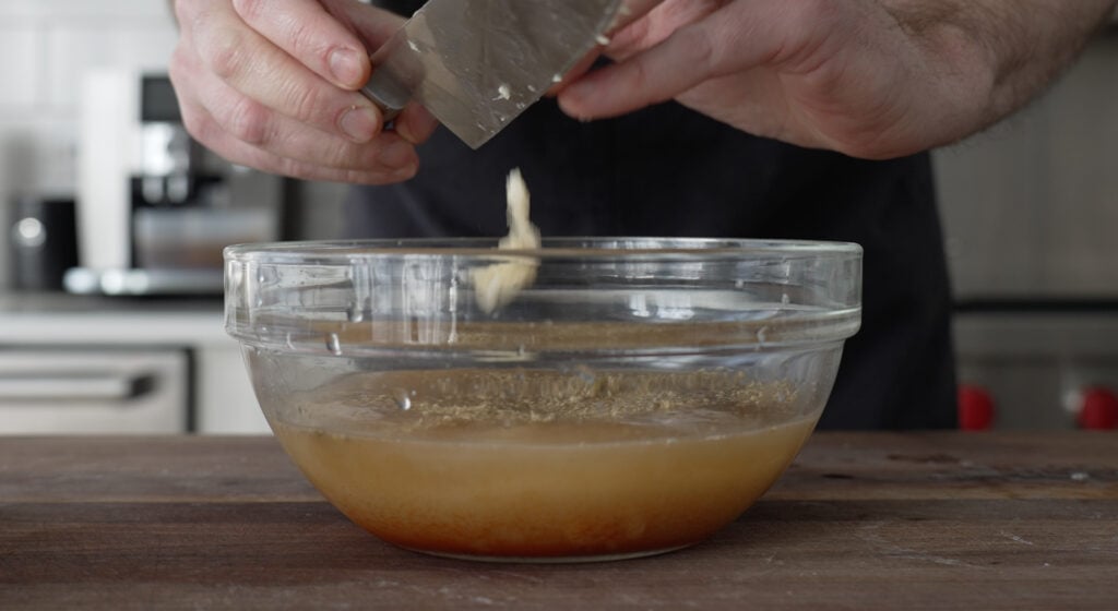 minced garlic falling from a knife into a glass bowl containing marinade ingredients