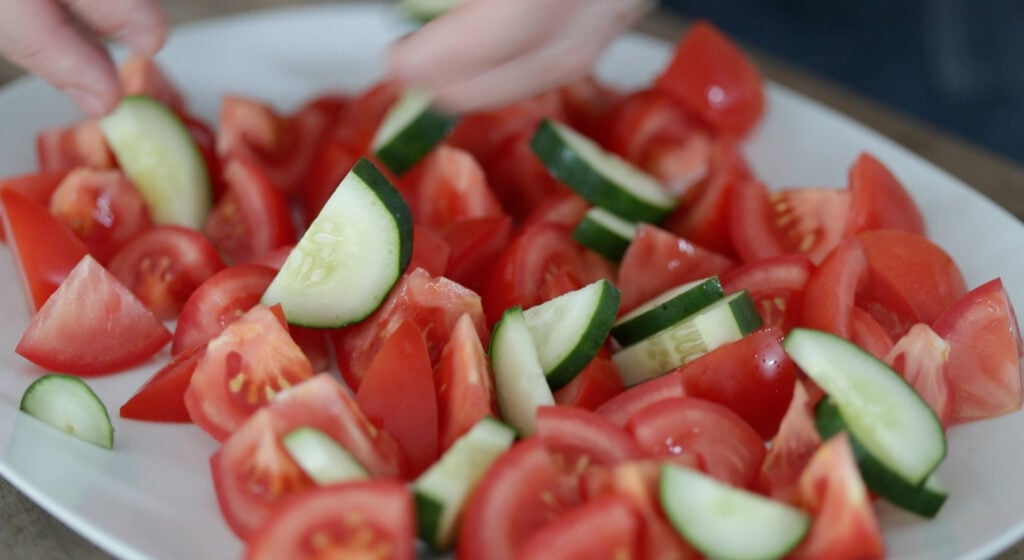 adding tomatoes and cucumbers to a platter