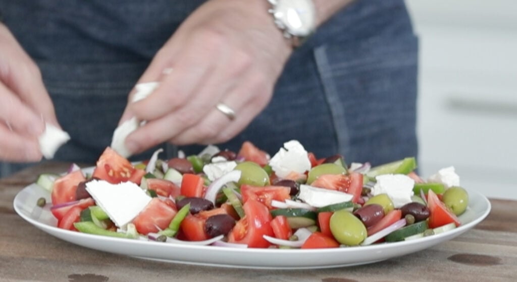 putting feta cheese chunks on an horiatiki salad