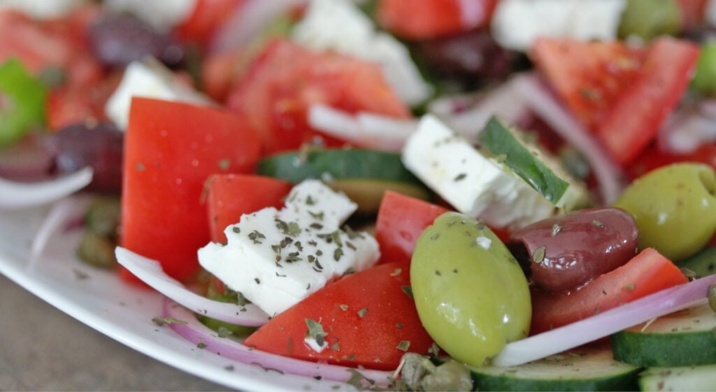 sprinkling herbs and olive oil on a Greek salad