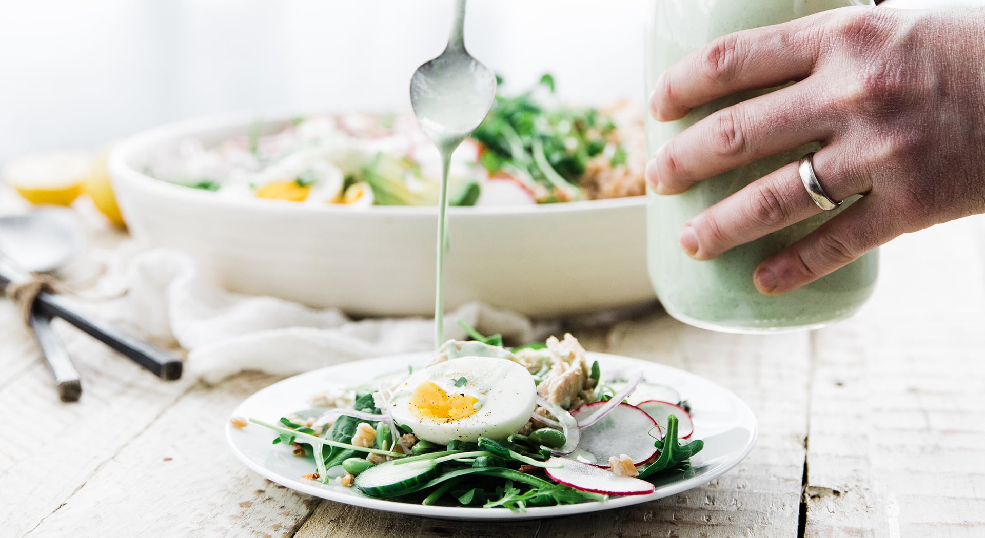 pouring dressing on a green goddess salad