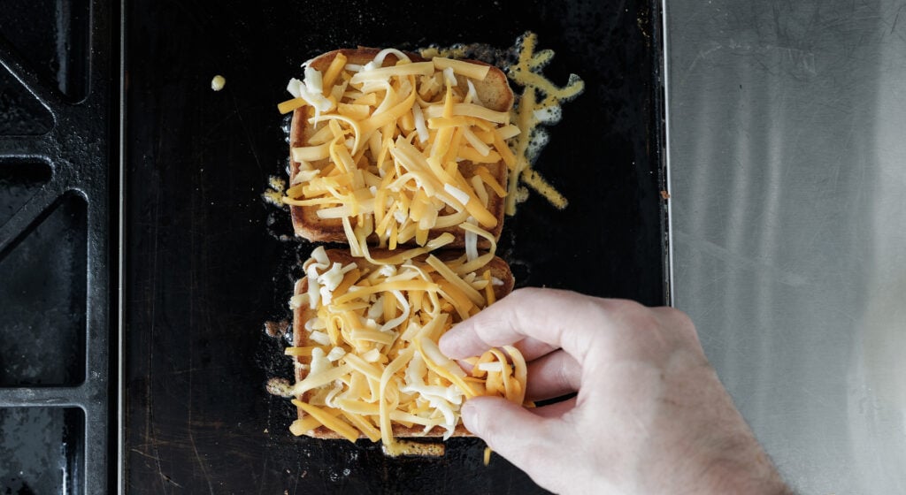 sprinkling shredded cheese on top of pieces of bread on a griddle.