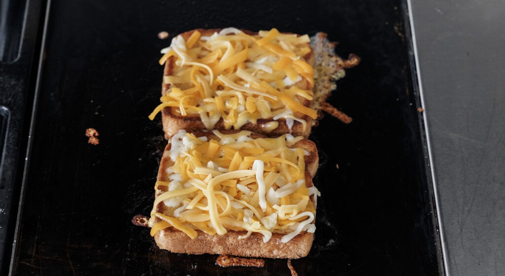 two pieces of cheese topped bread next to each other on the griddle