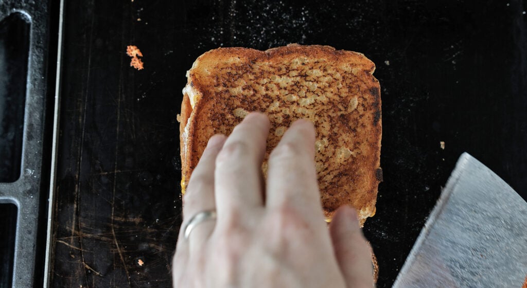 Using a metal utensil to move the grilled cheese off the griddle