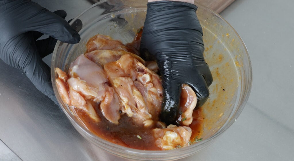 Using a gloved hand to mix the chicken thighs with the marinade