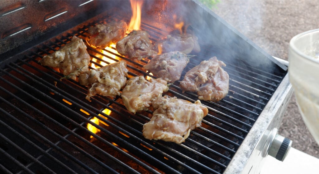 9 Chicken thighs on a grill with flames coming up from the grate