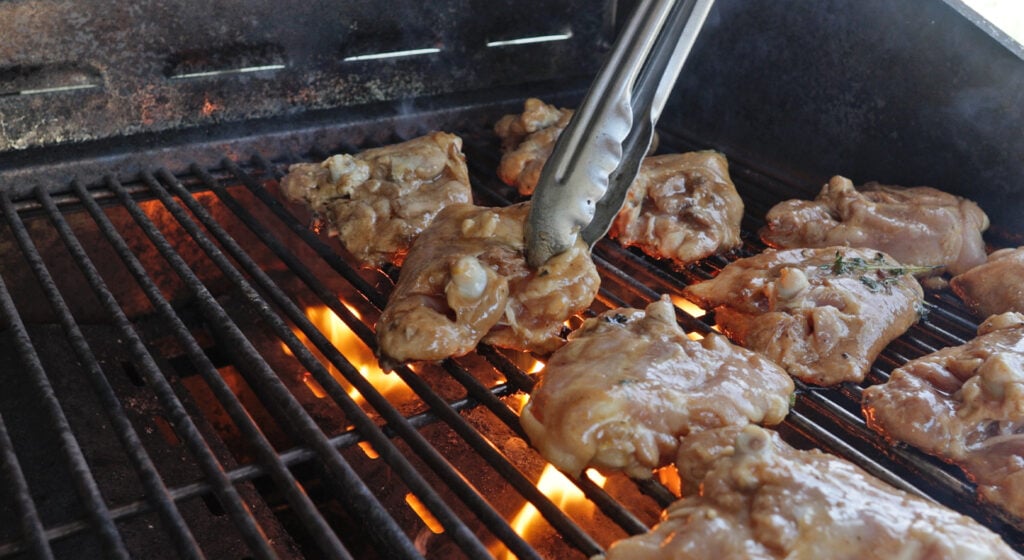 using tongs to turn a chicken thigh on a grill