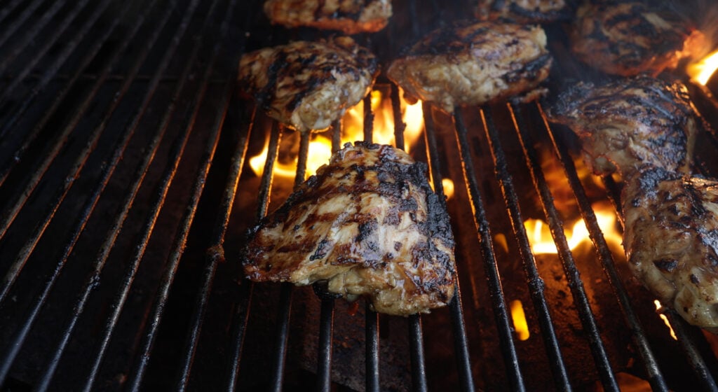 chicken thigh with grill marks on a grill with flames under