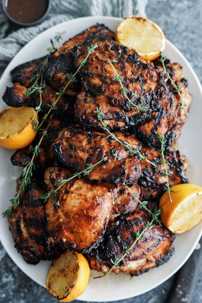 Grilled chicken thighs with slices of grilled lemons on a serving platter
