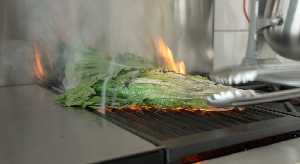 Romaine on a hot grill with flames coming up under the lettuce