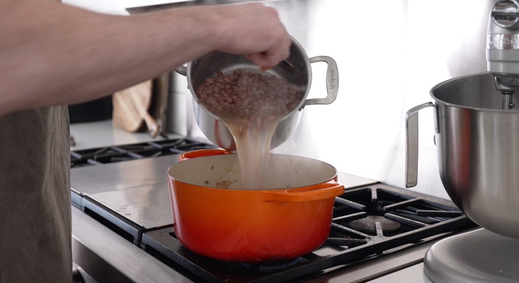 Pouring the beans and liquid into a pot on the stove
