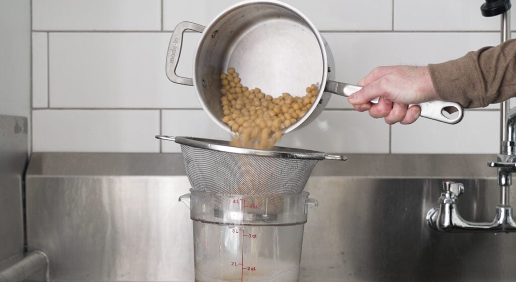 pouring chickpeas into a strainer set over a large container