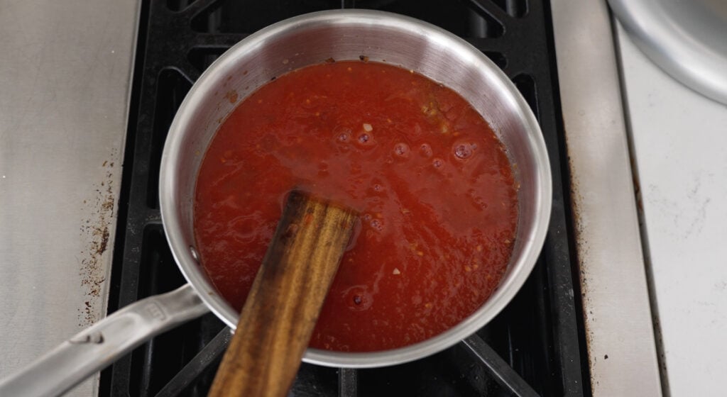 red tomato based sauce simmering in a pot with a wooden spoon resting in it