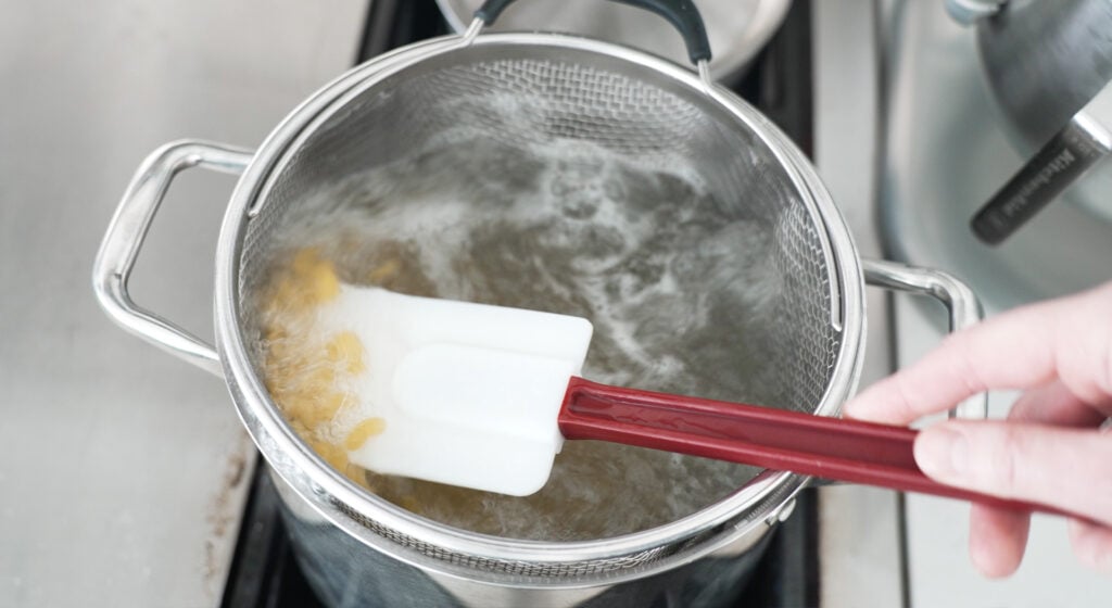 Rubber spatula scooping up cooked pasta in a pot