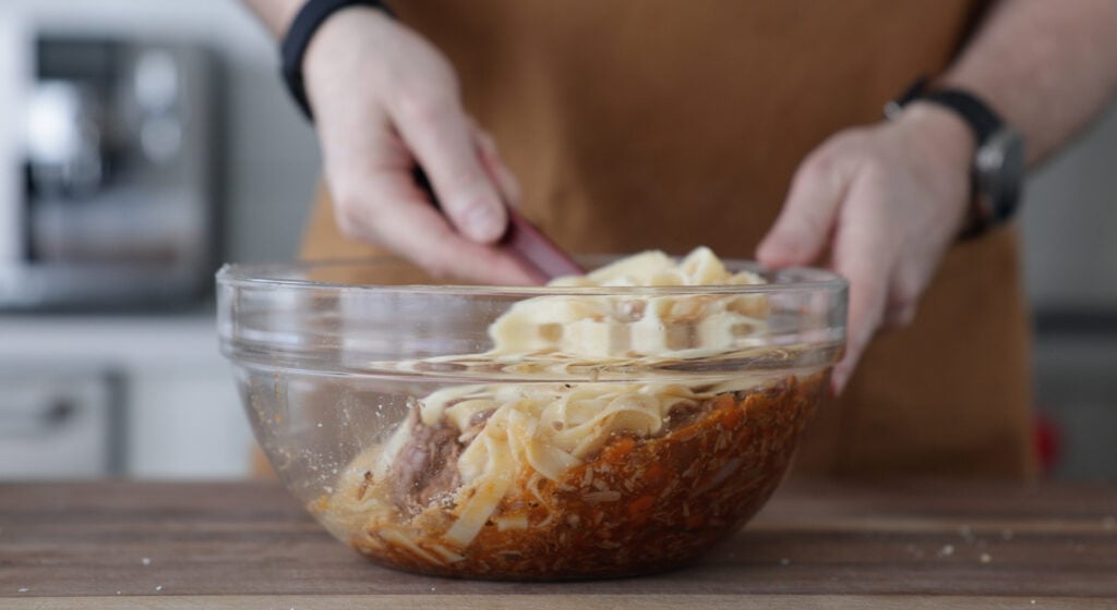 a glass bowl filled with lamb ragu and pasta being stirred with a kitchen utensil