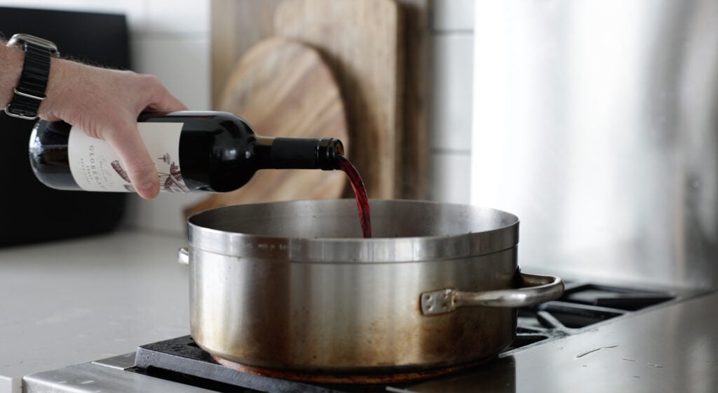 pouring red wine into a large rondeau on a stove