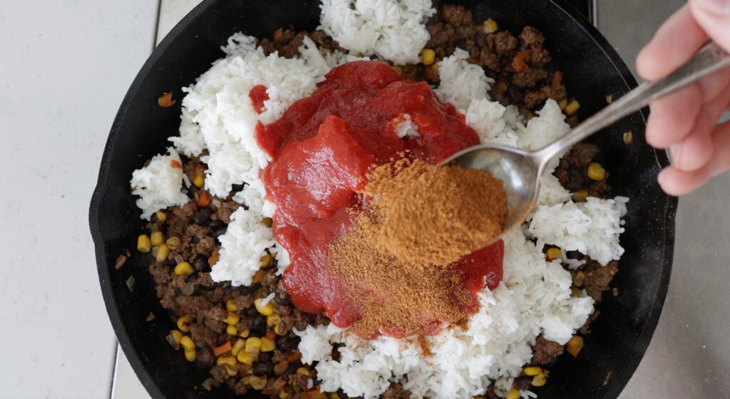 Close up of a spoonful of mexican spice blend over the skillet with ingredients